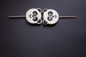 2 candies in the shape of a panda lies on top on a black background. Copy spase