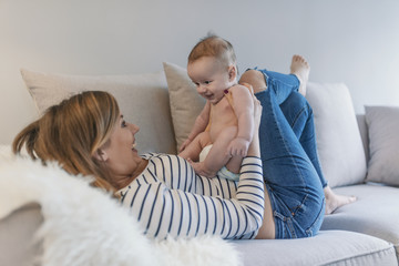  Mother and baby kissing, laughing and hugging.  Mom and baby boy in diaper playing in sunny living room.