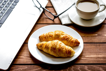 Business lunch with croissant and laptop on wooden desk