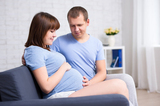 portrait of young beautiful pregnant couple sitting on sofa
