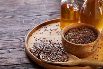Flax seeds in bowl and flaxseed oil in glass bottle on wooden background, top view, close-up, selective focus