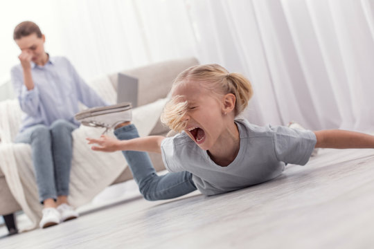 Awful behavior. Mischievous little blond girl shouting while lying on floor and demanding toy