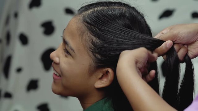 Woman plaits the braid of her little daughter
