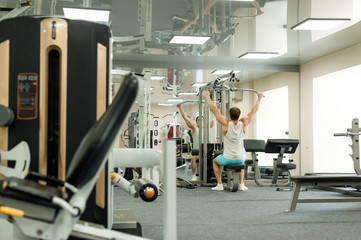 Fototapeta premium Young sexy male bodybuilder athlete, trains in the gym, using sports equipment and fitness equipment to improving health and beauty of the body