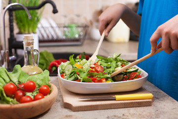 Kid hands mixing vegetable chunks into a delicious salad