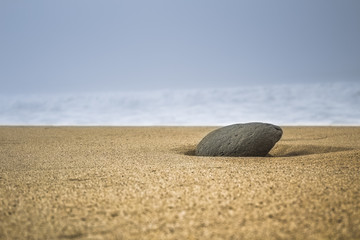 Fototapeta na wymiar single stone in sand on the beach