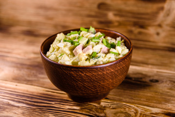 Ceramic bowl with russian traditional salad olivier on wooden table