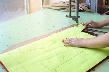 Female worker on a sewing manufacture uses electric cutting fabric machine.