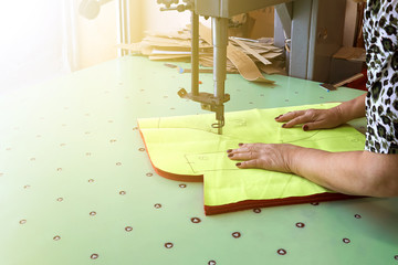 Female worker on a sewing manufacture uses electric cutting fabric machine.
