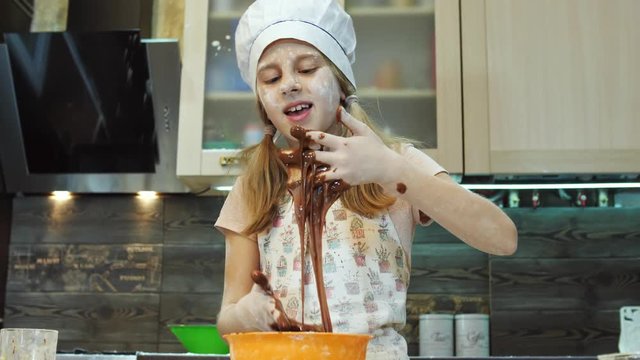Pretty kid having fun in the kitchen play and mixing chokolate dough with hands.