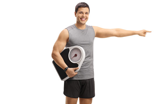 Young man in sportswear holding a weight scale and pointing