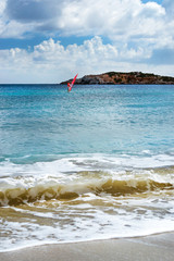 Windsurf with red sail rides on sea on background rocky shore. View from sunny Livadi beach in...
