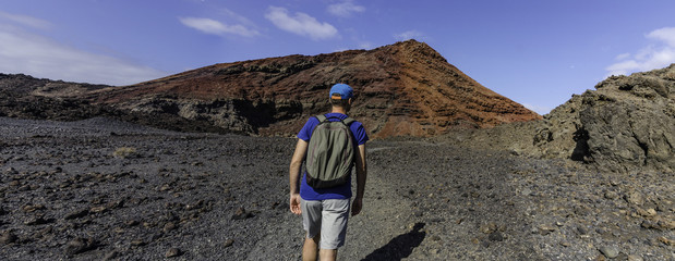 A man with a backpack trekking in volcanic landscape of Timanfaya National Park on Lanzarote, the...