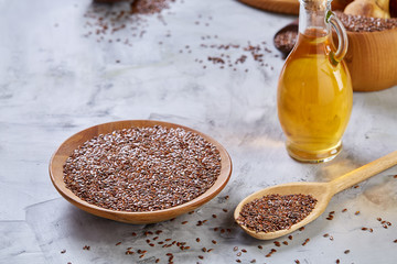 Flax seeds in bowl and flaxseed oil in glass bottle on wooden background, top view, close-up, selective focus