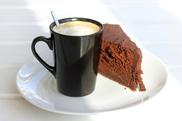 warming sweet dessert/ piece of chocolate cake with a frothy cappuccino on the table in the sunny morning