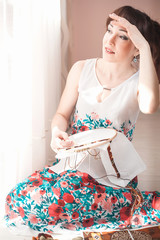 Young beautiful woman is engaged in embroidering a dagger on the embroidery frame in a colored...