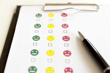 Customer service evaluation survey with smiley faces and pen.