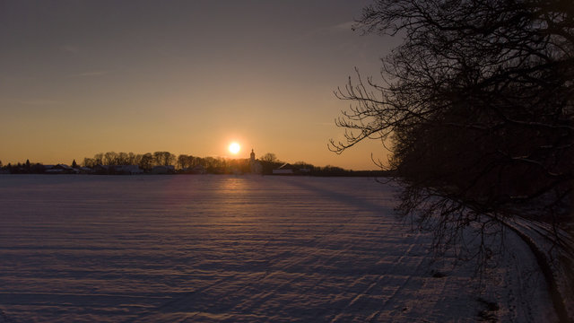 Sonnenuntergang mit verschneitem Dorf in Bayern