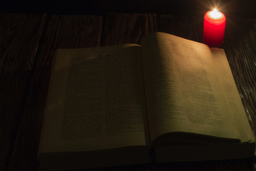 candle and a book of the Bible on wooden background at night