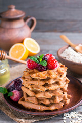 Homemade oatmeal waffles with berries and honey on a old wooden table