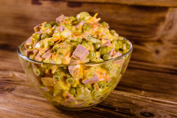 Salad with sausage, green pea, onion and carrot in glass bowl on wooden table