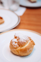 Choux cream puff with vanilla stuff icing on top for coffee break on white plate. Vertical food shot