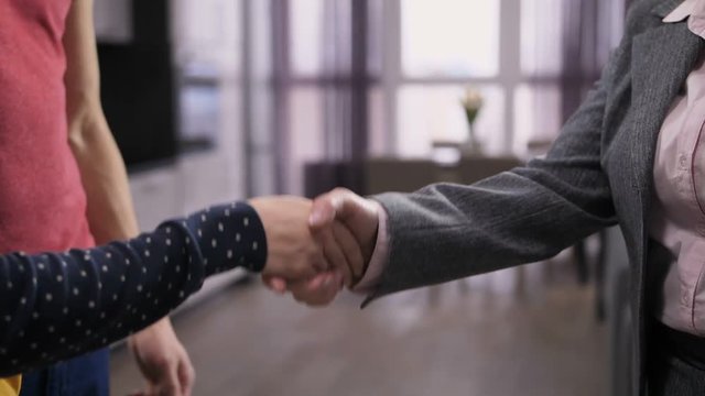 Close-up male hands clasping new home keys and female owner's handshake with real-estate agent. Midsection of happy couple getting new apartment keys from female realtor. Slow motion