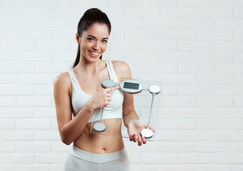 Beautiful, fit, young woman holding a weight scale, over a white brick wall