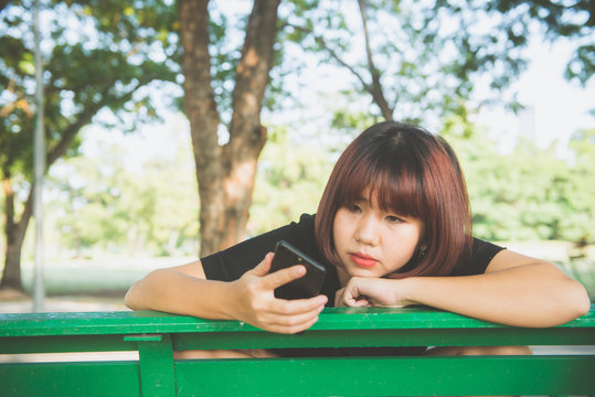 Cute asian woman reading pleasant text message on mobile phone while sitting in park spring day. Asian woman using on smart phone with feeling relax and smiley face. Lifestyle and technology concepts.