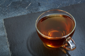 A glass cup of black tea with cookies on a dark greyish marble background. Breakfast background