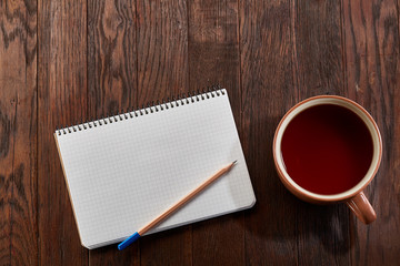 Cup of tea with cookies, workbook and a pencil on a wooden background, top view