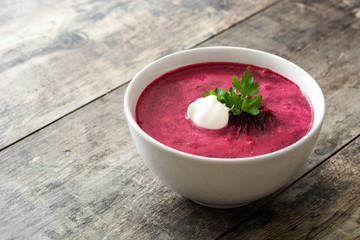 Beet soup in white bowl on wooden table