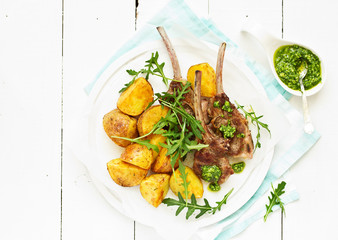 Chops of lamb on bone, with baked potatoes and pesto sauce.