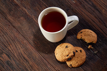 Cup of tea with cookies, workbook and a pencil on a wooden background, top view
