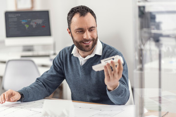 Nice one. Joyful young engineer holding a recently printed 3D model and scrutinizing it, checking...