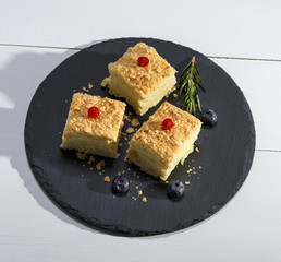 three slices of Napolon pie with cream on a black plate