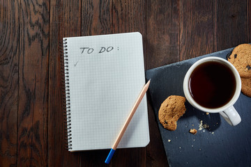 Cup of tea with cookies, workbook and a pencil on a wooden background, top view