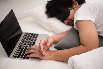 Asian man is sleeping on the bed in bedroom leave his work on computer.