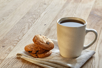 Porcelain teacup with chocolate chips cookies on cotton napkin on a rustic wooden background, top view