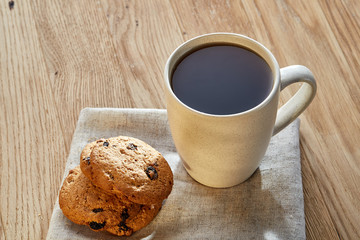 Porcelain teacup with chocolate chips cookies on cotton napkin on a rustic wooden background, top view