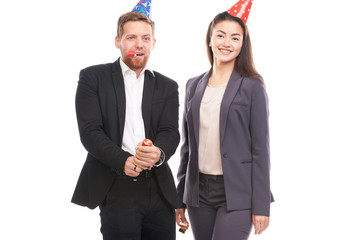 Portrait of male and female office workers wearing party hats and blowing into horn blowers