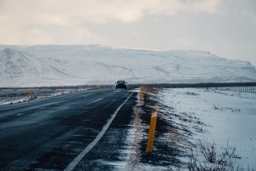 Winter road in snow blizzard. Blowing snow across the road. Difficult driving conditions in winter season in Iceland. Sunny but windy day, typical Icelandic route troubles. Icelandic safety driving.
