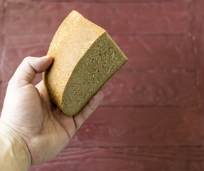 A piece of black bread in hand on a claretish wooden background.