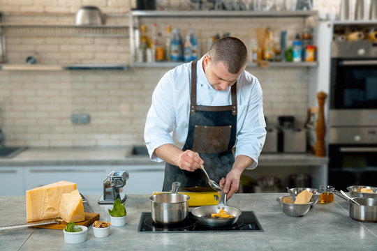 chef in apron stirring ravioli pasta in frying pan on burner in restaurant kitchen