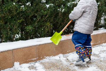 Child helping clearing snow from sidewalk. Candid authentic family winter activities. Snow...