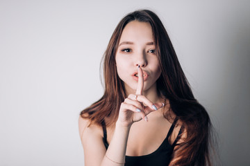 Beautiful girl with long hair holds a finger on her mouth a secret
