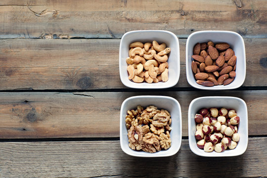 Four kinds of nuts in white bowls.