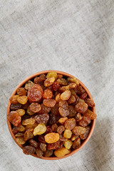 Wooden bowl with golden raisins on light tablecloth, close-up, selective focus