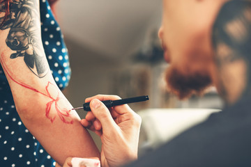 A young guy, a tattoo artist preparing for the session, draws a sketch on the body of the client in...