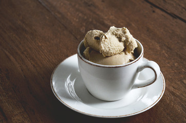 White coffee cup filled with soft coffee flavoured ice cream on dark wooden background